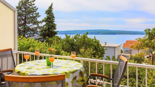 Een balkon met een tafel voor twee personen, met uitzicht op een waterpartij en heuvels in de verte.
