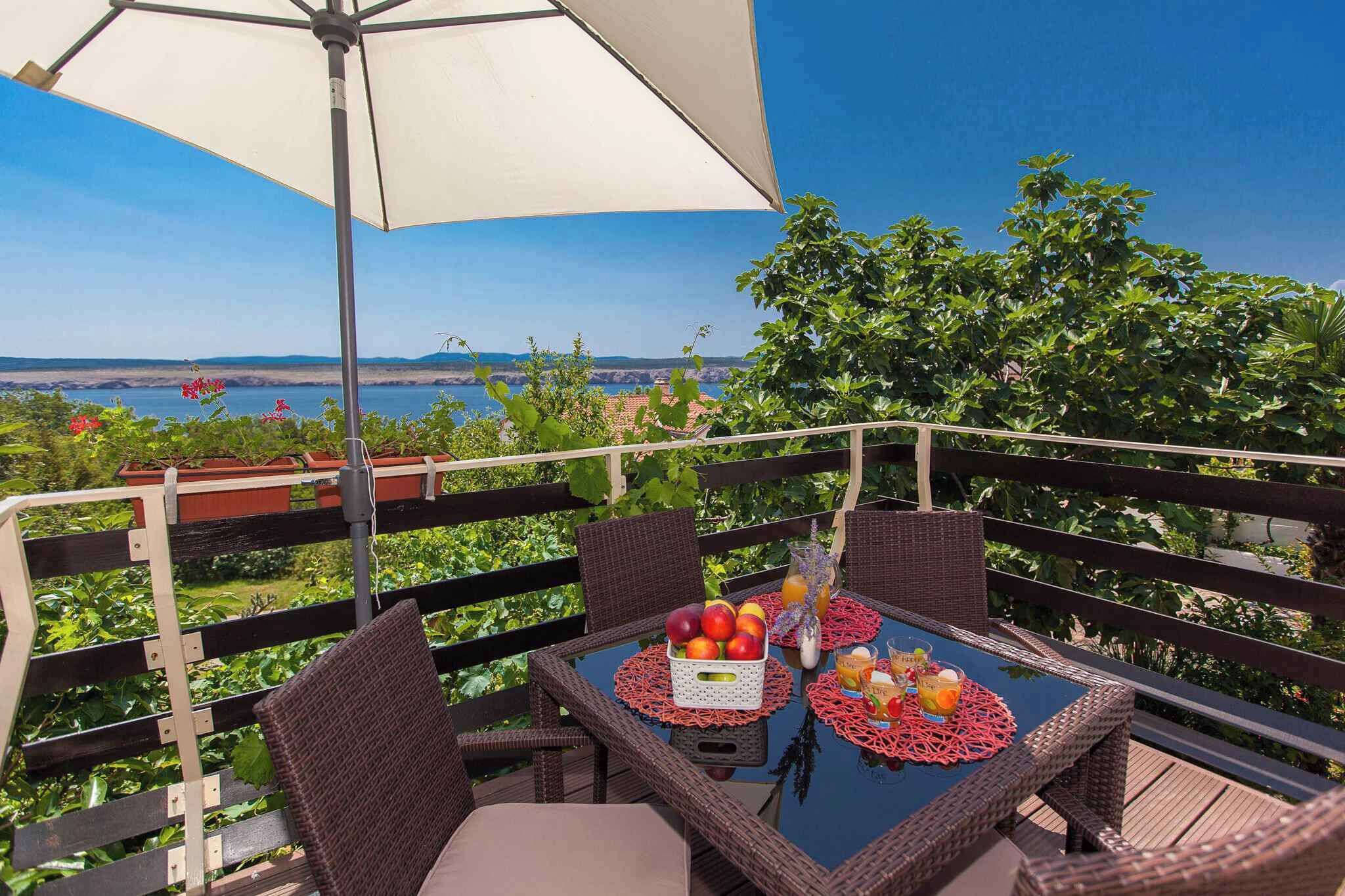Een tafel met rieten stoelen en een witte parasol, met uitzicht op zee en groen.