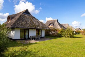 A modern house with a thatched roof, a patio with outdoor furniture, and a well-maintained lawn.