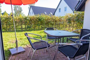 Eine Terrasse mit Tisch und Stühlen, einem roten Sonnenschirm und Blick auf ein Haus und einen Garten.