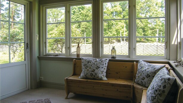 A cozy room with a wooden bench and two pillows, large windows with a view of trees and a wooden deck outside. - Stunning home in Lidhult with WiFi (Lidhult)