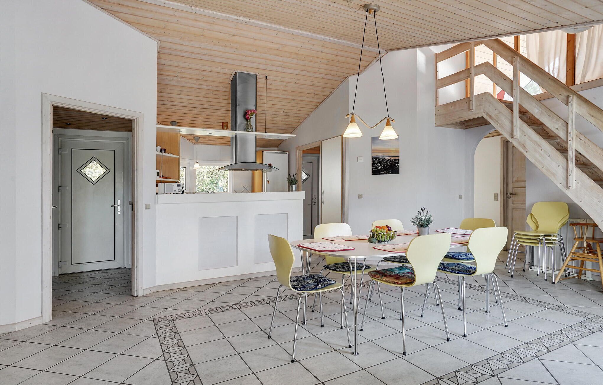 A modern kitchen with a central island, a dining area with a round table and chairs, and a wooden staircase.