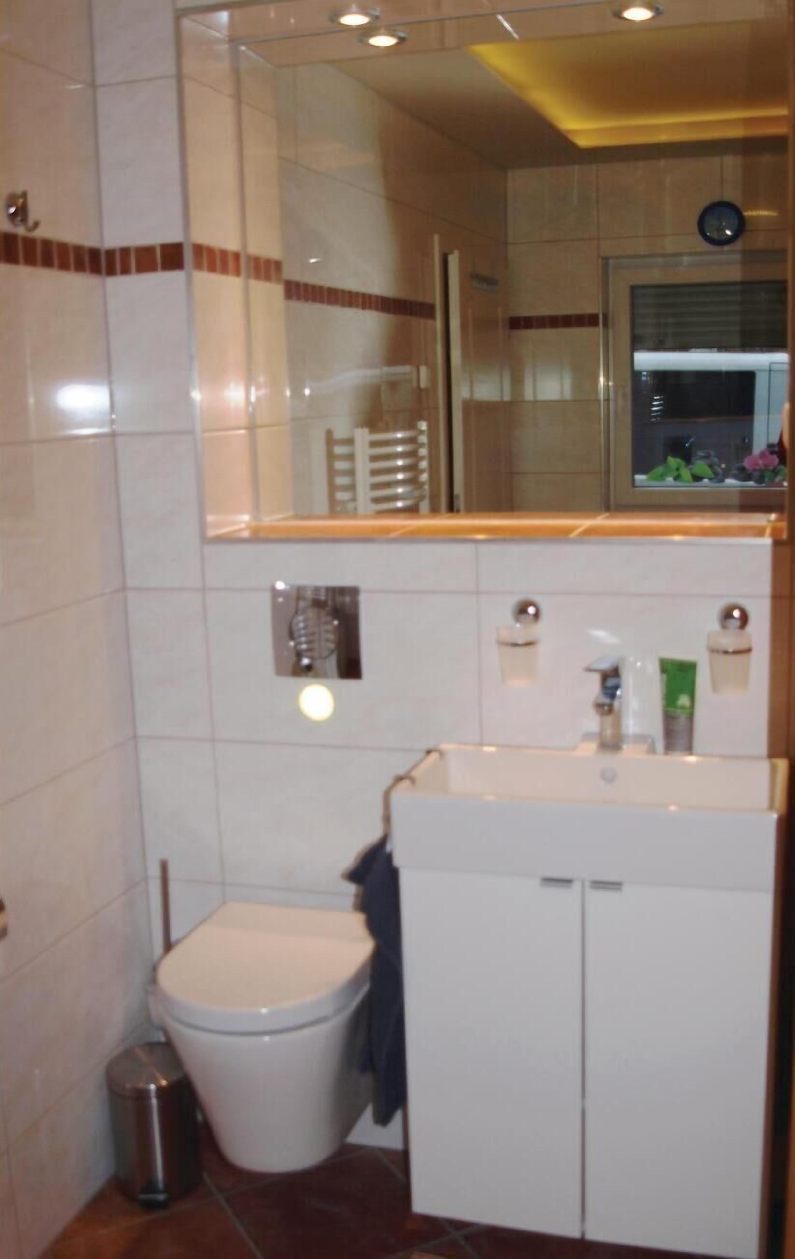 A bathroom with a toilet, sink, mirror, and cabinet.