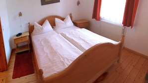 A double bed with white linens, a wooden headboard, a nightstand with a lamp, and a red rug on a wooden floor. - Apartment 2 - Rügen apartment 106 (Wiek)