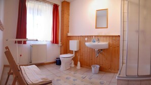 A bathroom with a toilet, sink, shower, wooden paneling, and a radiator. - Apartment 2 - Rügen apartment 106 (Wiek)