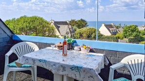 En balkong med ett bord dukat för två personer, med utsikt över en kuststad med hus och havet.