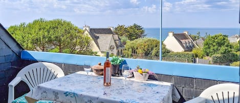 A balcony with a table set for two, overlooking a coastal town with houses and the sea.