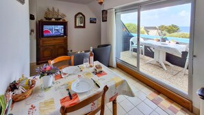 En matplats med ett bord dukat för två personer, en tv-apparat på ett träskåp och utsikt över havet genom en skjutdörr i glas.