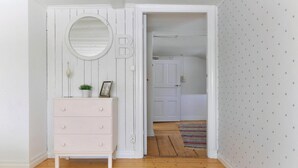 Une pièce avec une commode blanche, un miroir rond et une porte donnant sur une autre pièce dont le mur est décoré de motifs en forme d’étoiles.