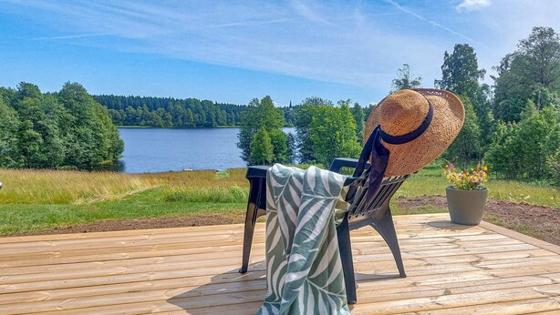 Une terrasse en bois avec une chaise et une table, d’où l’on a vue sur un lac et une forêt.