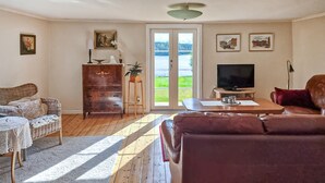 Un salon avec un canapé marron, des meubles en osier, un meuble en bois, un téléviseur et une vue à travers des portes vitrées.