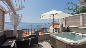 A balcony with a hot tub, outdoor furniture, and a view of the sea.