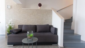 A modern living room with a dark grey sofa, a small round table with a glass vase, a potted plant, and a staircase with grey steps.