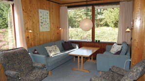 Un acogedor interior de cabaña con un sofá, dos sillones, una mesita y una ventana con cortinas.