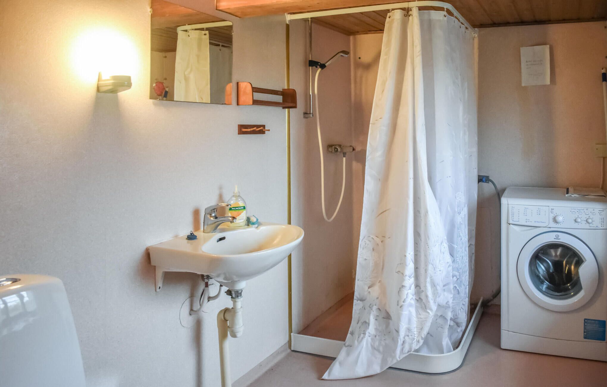 Une petite salle de bain avec un lavabo, une douche avec un rideau et un lave-linge.