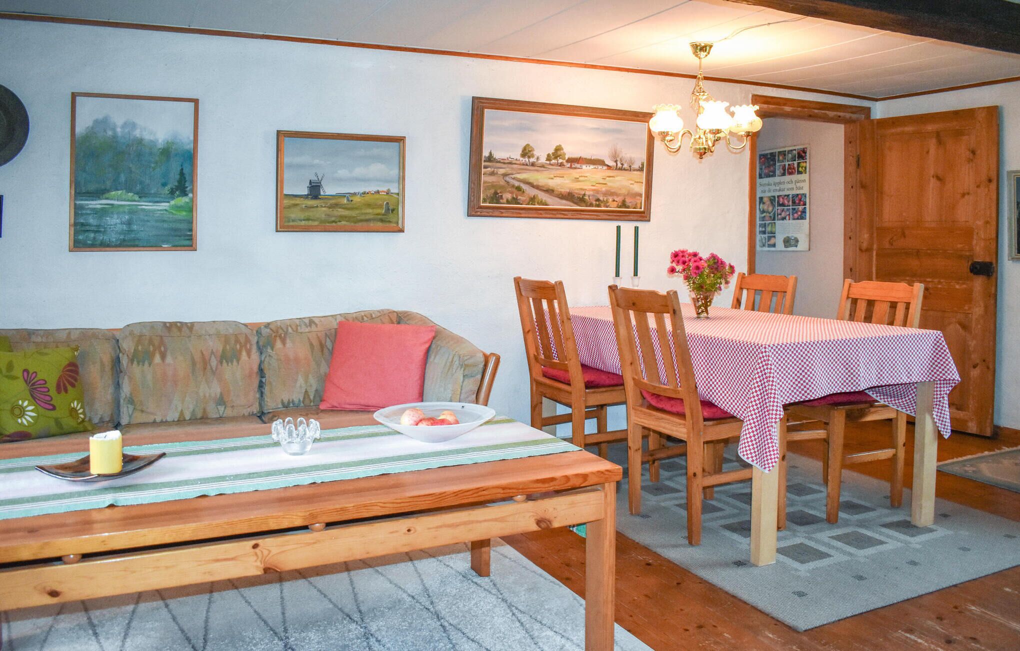 A cozy dining area with a wooden table, chairs, and a bench. There are paintings on the wall and a chandelier above the table.