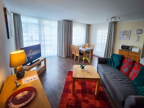 En stue med fjernsyn, sofa, sofabord og spiseområde med stole og bord.