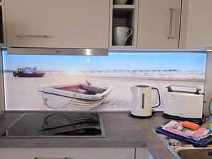Une cuisine dotée d’une grande fenêtre donnant sur une plage, avec une bouilloire, un grille-pain et un évier.