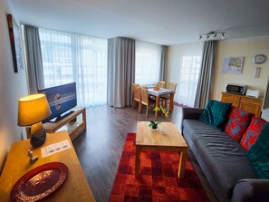 Un salon comprenant un téléviseur, un canapé, une table basse et un coin repas avec des chaises et une table.
