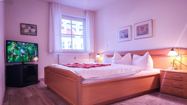 Ein Hotelzimmer mit Bett, Fernseher, einem Fenster mit Vorhängen und einem Nachttisch mit Lampe.