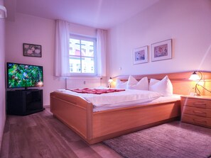 Ein Hotelzimmer mit Bett, Fernseher, einem Fenster mit Vorhängen und einem Nachttisch mit Lampe.