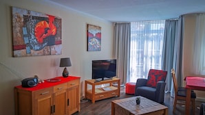 Ein Wohnzimmer mit Fernseher, Holzmöbeln, einem roten Teppich und Kunstwerken an den Wänden.