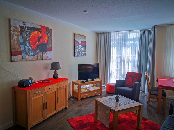 A living room with a TV, wooden furniture, a red rug, and artwork on the walls.