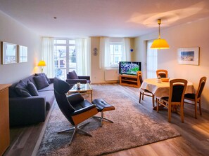 Un salon comprenant un canapé, un fauteuil, un téléviseur, une table à manger, des chaises et un tapis.