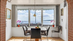 Un comedor con una mesa redonda, cuatro sillas y vista al mar a través de amplios ventanales.