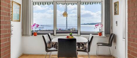 Un comedor con una mesa redonda, cuatro sillas y vista al mar a través de amplios ventanales.