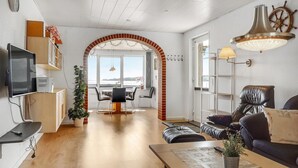 Una sala de estar moderna con televisor, comedor y vista al mar.