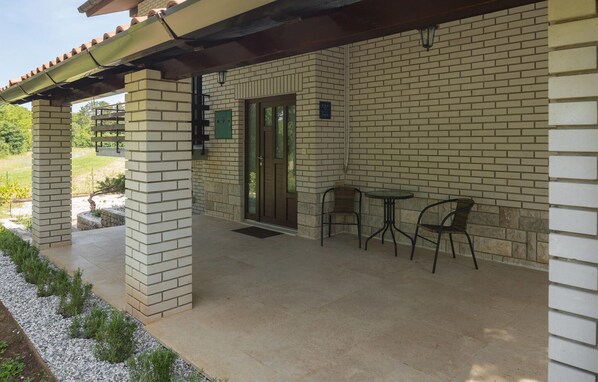 A covered patio area with a brick wall, a door, and two metal chairs.