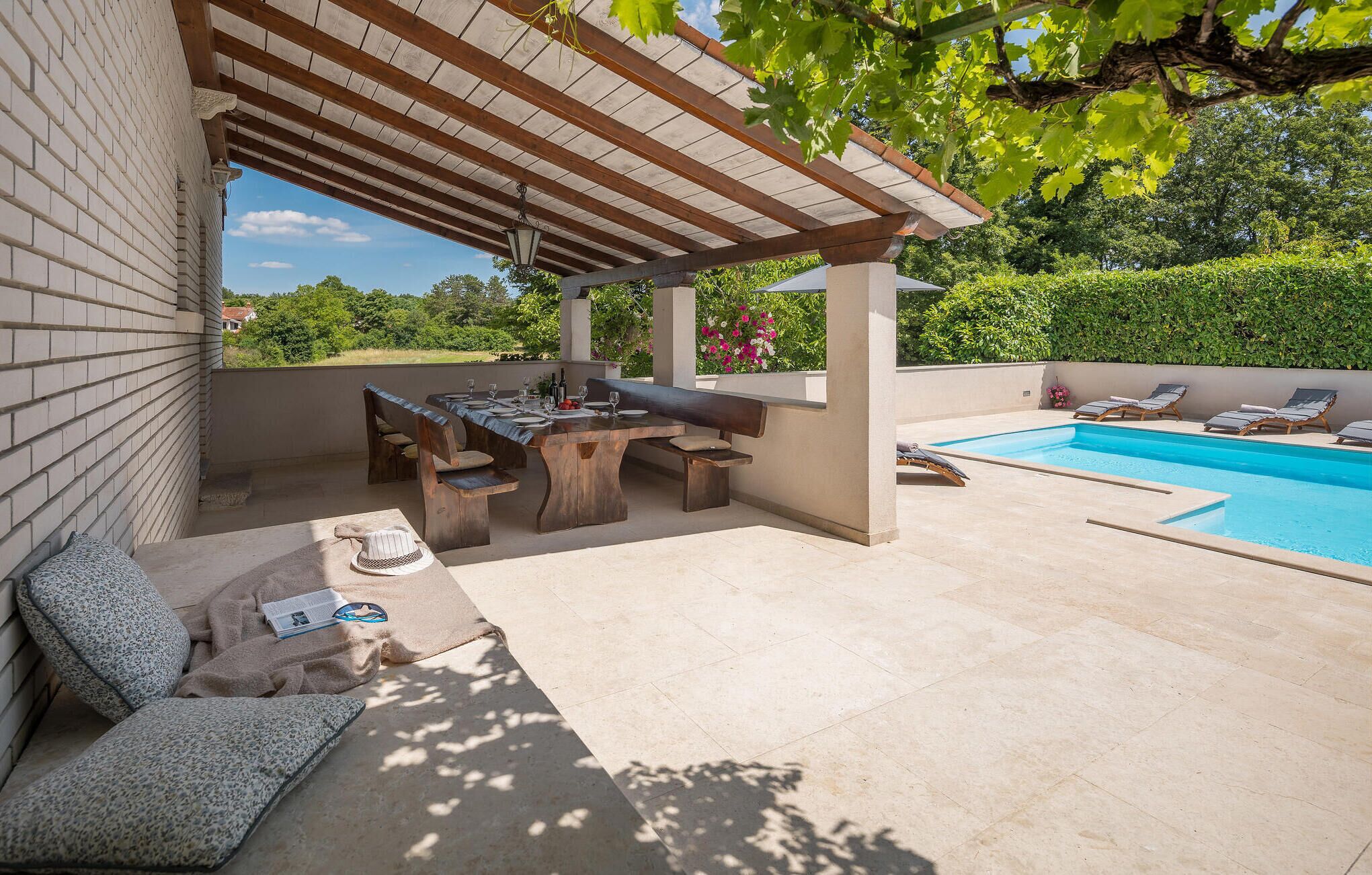 A covered outdoor area with a pool, a dining table with chairs, and a seating area with cushions.