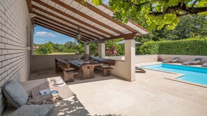 Un espace extérieur abrité comprenant une piscine, une table à manger avec des chaises et un coin salon avec des coussins.