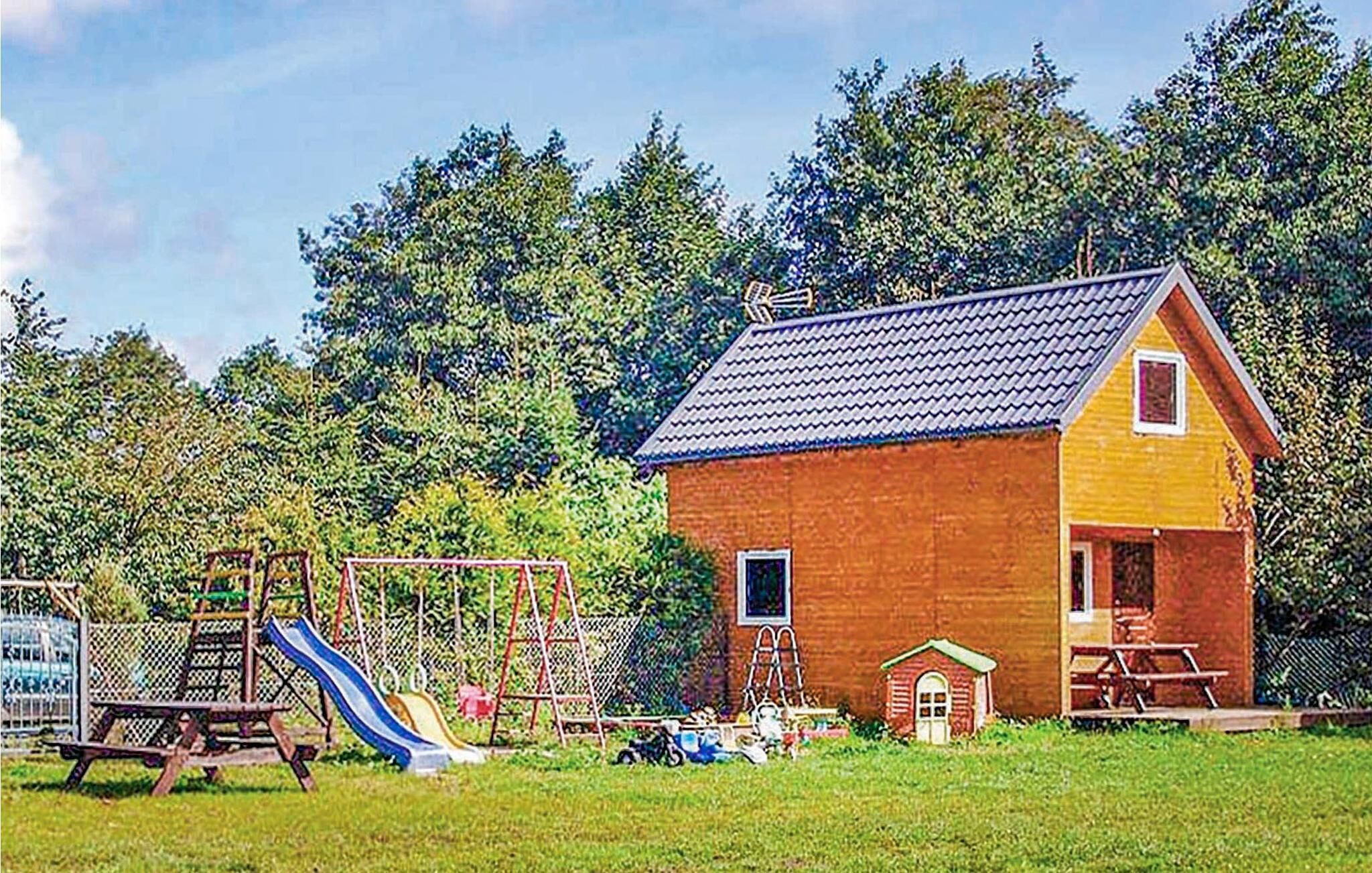 Una pequeña casa de ladrillo con techo rojo, un porche pequeño y un tobogán en un patio cercado.