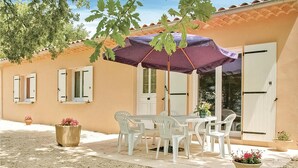 A patio with a table and chairs under a purple umbrella, surrounded by potted plants and a building with white shutters. - 3 bedroom nice home in Saint-Thomé (Saint-Thomé)