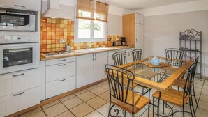 A kitchen with white cabinets, a gas stove, a double oven, a window with blinds, a coffee maker, and a dining table with chairs. - 3 bedroom nice home in Saint-Thomé (Saint-Thomé)