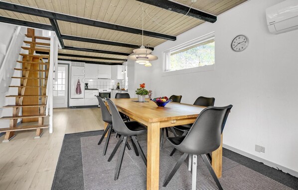 A modern kitchen with white cabinets, a wooden staircase, and a dining area with a wooden table and black chairs. - Lovely home in Rømø with kitchen (Rømø)