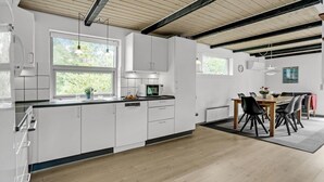 Een moderne keuken met witte kastjes, een houten eettafel en uitzicht op groen.
