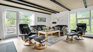 Een moderne woonkamer met leren banken, een houten salontafel en grote ramen met uitzicht op groen.