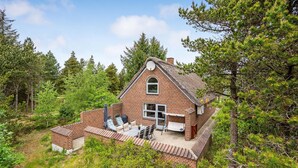 Een rustiek, met baksteen opgetrokken huis met schoorsteen, omgeven door dicht bos.