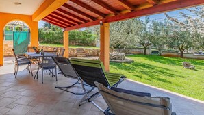 Eine überdachte Terrasse mit Gartenmöbeln und Blick auf einen angelegten Garten.