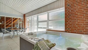 Ein Whirlpool in einem Zimmer mit Backsteinwand, großen Fenstern und einem Essbereich mit Stühlen und Tisch.