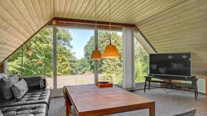 Ein gemütliches, modernes Wohnzimmer mit schrägverdeckter Decke, einem großen Fernseher und einer bequemen Couch.