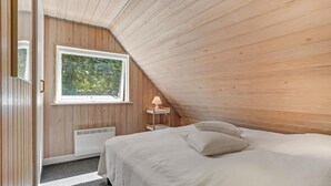 Ein Schlafzimmer mit schrägen Wänden, einem Fenster, einem Nachttisch und einem Bett.