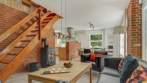 Ein gemütliches Wohnzimmer mit Kamin, einer Holztreppe und einem Essbereich mit Tisch für zwei Personen.