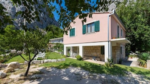Ein zweistöckiges Haus mit Naturstein-Fassade, grünen Fensterläden und einer überdachten Terrasse.