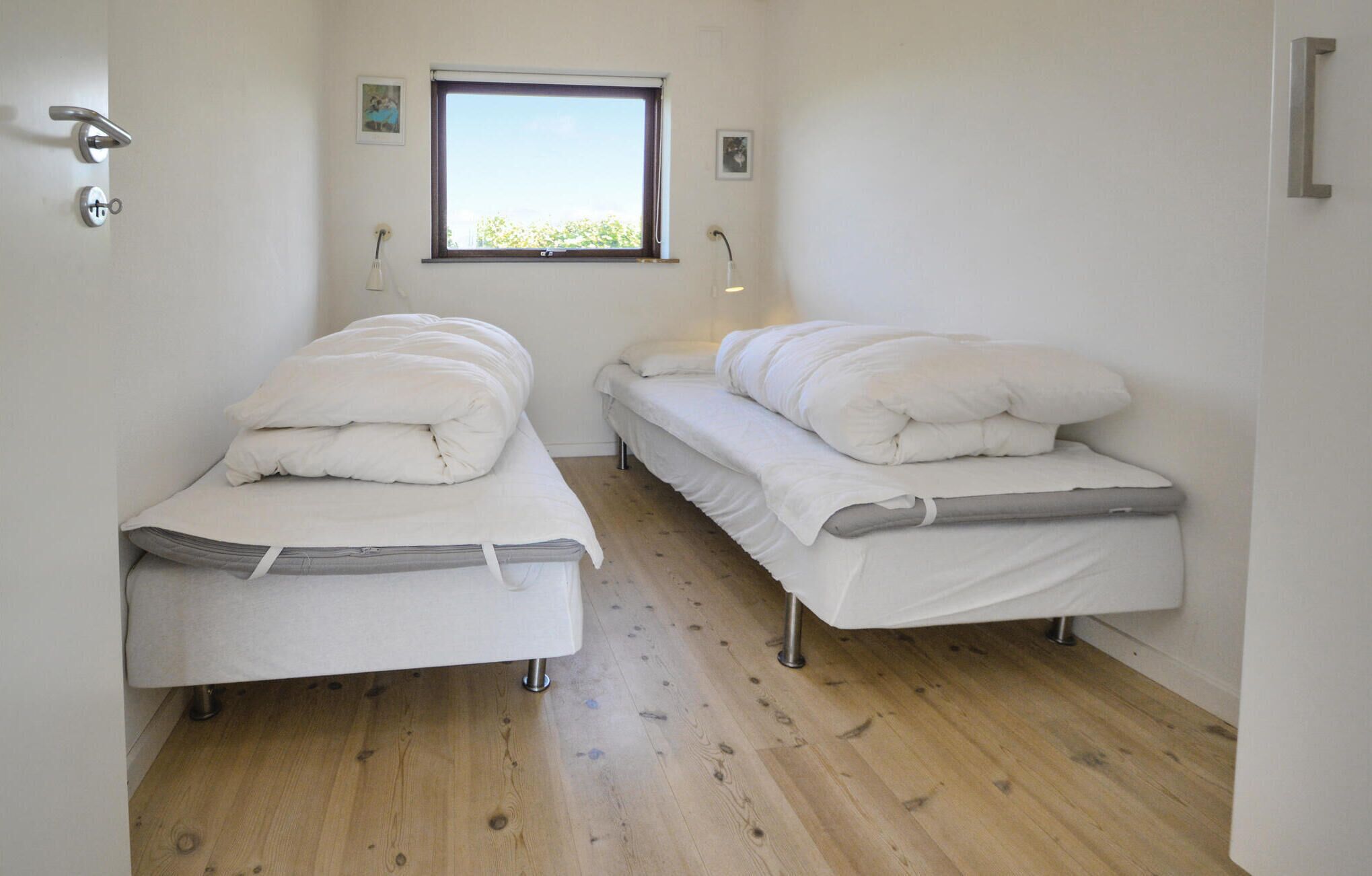 Une petite chambre propre, avec deux lits simples, une fenêtre et une porte dotée d’une poignée.