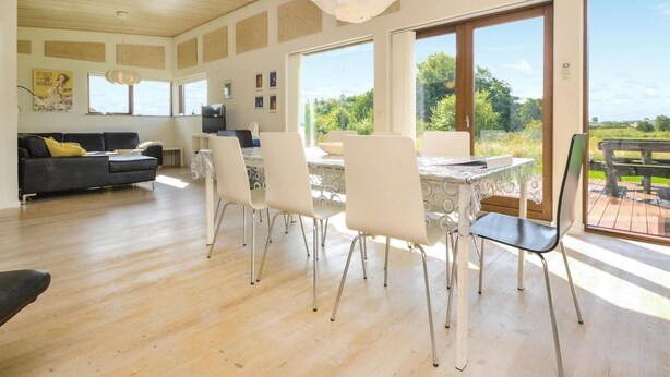 A spacious living area with a dining table, white chairs, and a sofa. There are large windows offering a view of the outdoors. - Beautiful home in Haderslev with WiFi (Haderslev)
