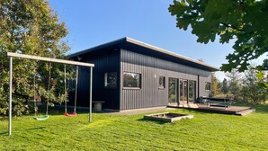 A modern building with a flat roof, large windows, and a patio area with a swing set. - Beautiful home in Haderslev with WiFi (Haderslev)